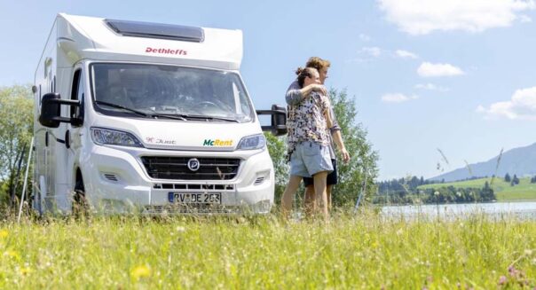 Een stel staat schuin voor de McRent Kiwi Compact camper te genieten van het uitzicht