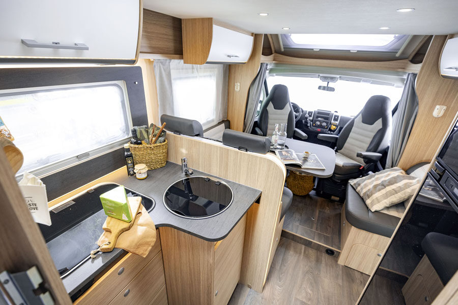Het interieur van de McRent Family Standard camper vanuit de keuken gezien kijkend naar voren waar de draaibare stoelen van de cabine omgedraaid staan naar de zithoek
