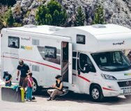 Een man staat met zijn twee kinderen naast de McRent Family Plus camper terwijl zijn vrouw op het opstapje bij de ingang van de camper zit