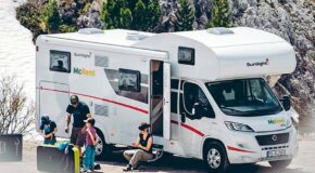 Een man staat met zijn twee kinderen naast de McRent Family Plus camper terwijl zijn vrouw op het opstapje bij de ingang van de camper zit