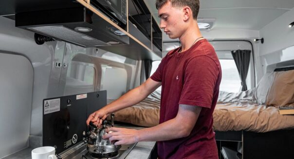 Jongen staat te koken in de Mighty Highball camper in Nieuw-Zeeland