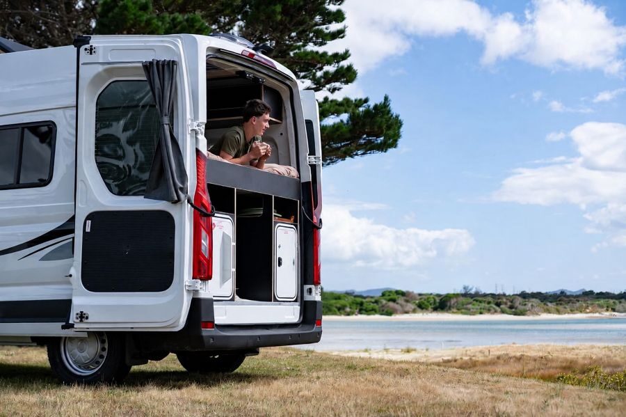 Man ligt op het bed van de Apollo Hitop camper met de achterdeur open en kijkt naar buiten