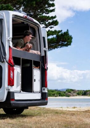 Man ligt op het bed van de Apollo Hitop camper met de achterdeur open en kijkt naar buiten