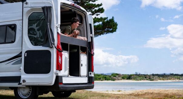 Man ligt op het bed van de Apollo Hitop camper met de achterdeur open en kijkt naar buiten