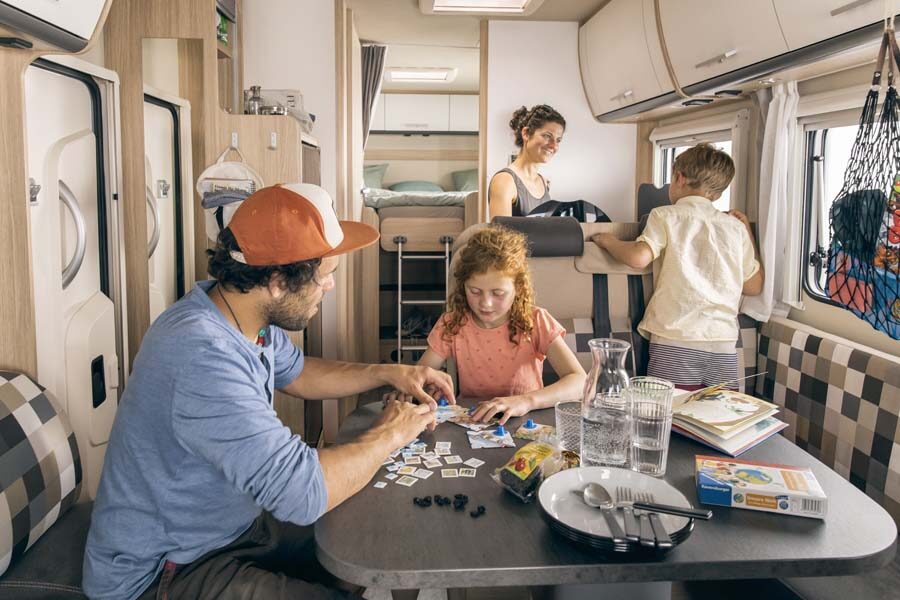 Een vader doet met zijn dochter in spelletje aan tafel in de McRent Family Luxury motorhome terwijl de vrouw in de keuken staat en naar haar zoon kijkt