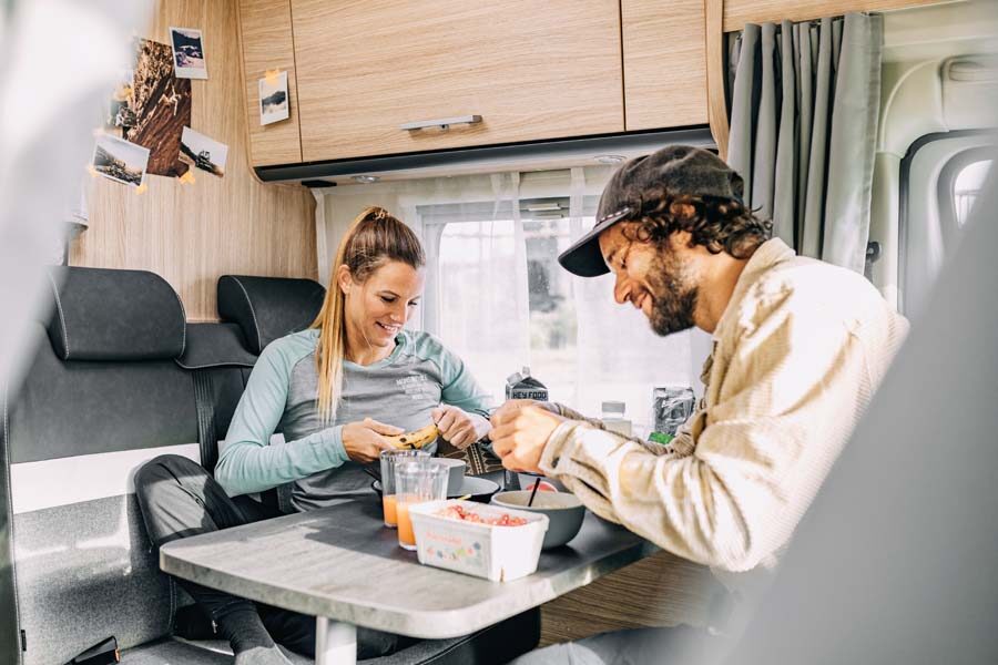Een koppel is aan het eten in de zithoek van de McRent Compact Plus camper