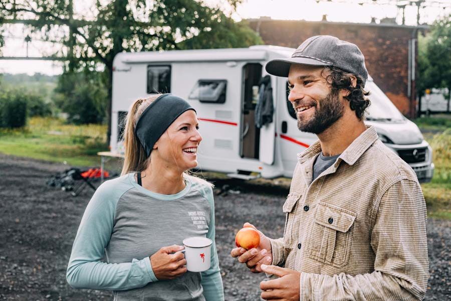 Een stel staat met wat drinken en een appel voor de geparkeerde McRent Compact Plus