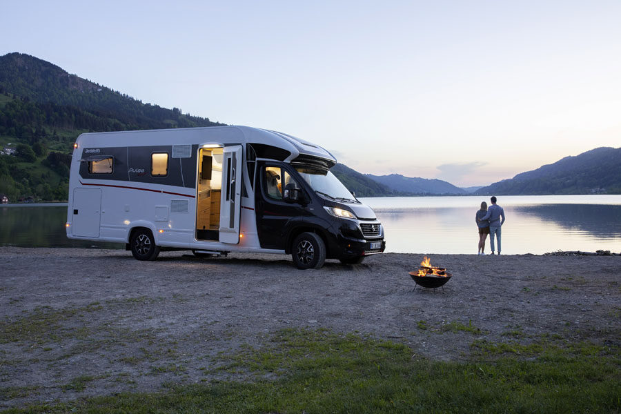 De McRent Comfort Standard camper staat geparkeerd aan een meer waar een koppel naast de camper naar de zonsondergang kijkt