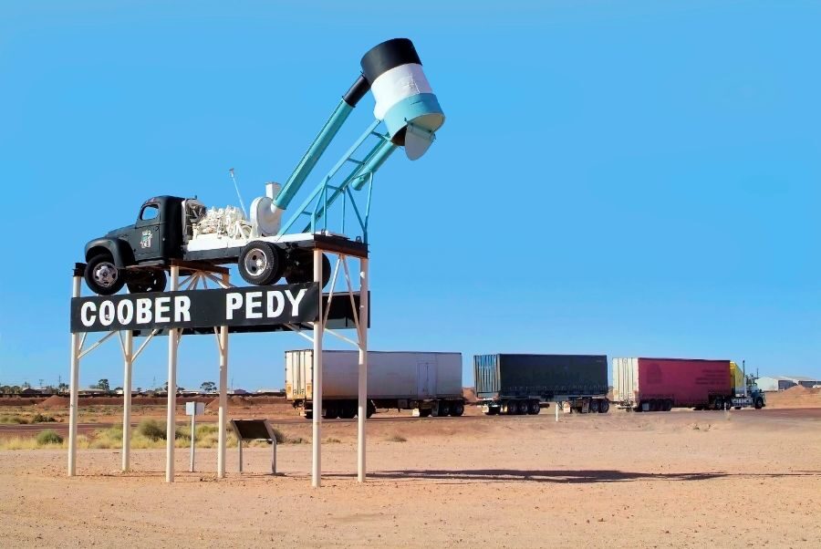 Plaatsnaambord van Coober Pedy met mijnbouw wagen erop en vrachtwagen op de achtergrond
