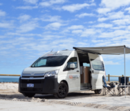 De RedSands camper op het strand met de zijdeur geopend en de campingtafel en stoelen onder de uitgeklapte luifel