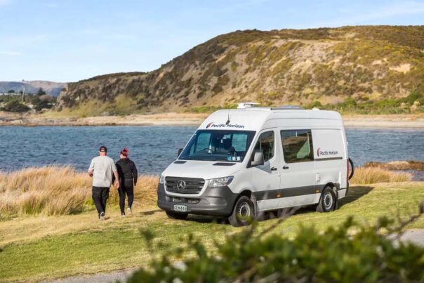 Een koppel loopt vanuit de Pacific Horizon 2 plus 1 camper naar een meer toe in Nieuw-Zeeland