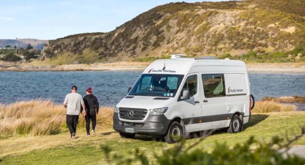 Een koppel loopt vanuit de Pacific Horizon 2 plus 1 camper naar een meer toe in Nieuw-Zeeland
