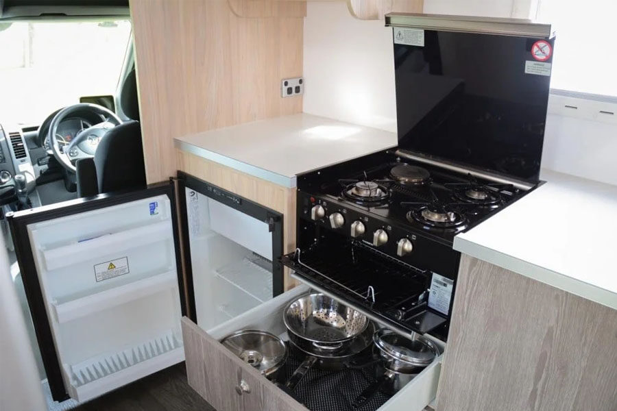 De keuken met drie gaspitten, opberglades en een open koelkast in de Pacific Horizon Max 4 camper