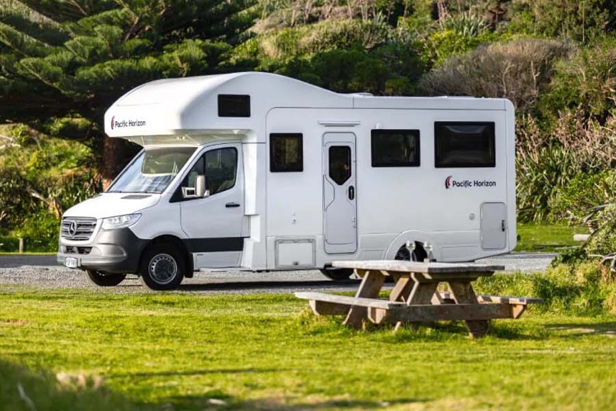 De zijkant van de Pacific Horizon Max 4 camper die geparkeerd staat naast een picknickbank