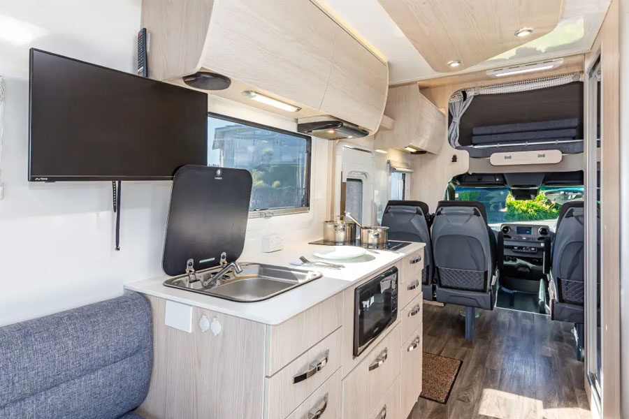 Het interieur van de Pacific Horizon Sam 6 camper kijkend van voor naar achter met TV, keuken en bijrijders stoelen