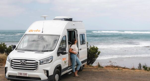 Vrouw staat tegen geopende zijdeur van Britz Trailblazer langs de Great Ocean Road
