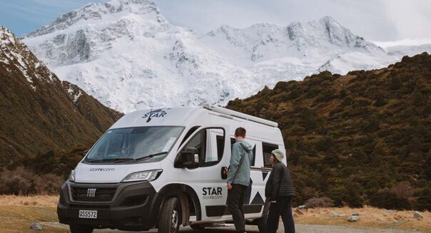 Een stel loopt naar de geparkeerde Star RV Polaris 2 camper met op de achtergrond besneeuwde bergtoppen