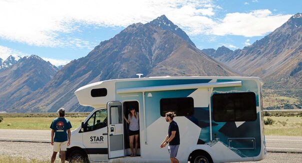 Een vrouw staat in de deuropening van de Star RV Polaris 6 camper en kijkt naar haar vrienden die genieten van het uitzicht