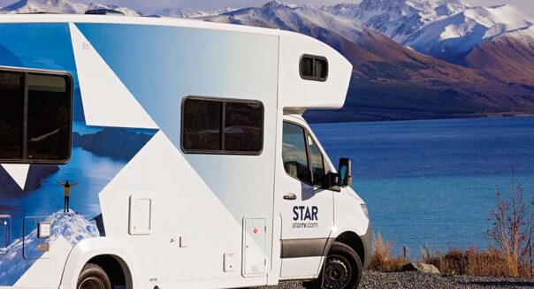 De zijkant van de Star RV Polaris 6 camper die geparkeerd staat naast een meer met uitzicht op besneeuwde bergtoppen