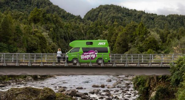 Een vrouw staat naast de op een brug geparkeerde Jucy Chaser camper in Nieuw-Zeeland
