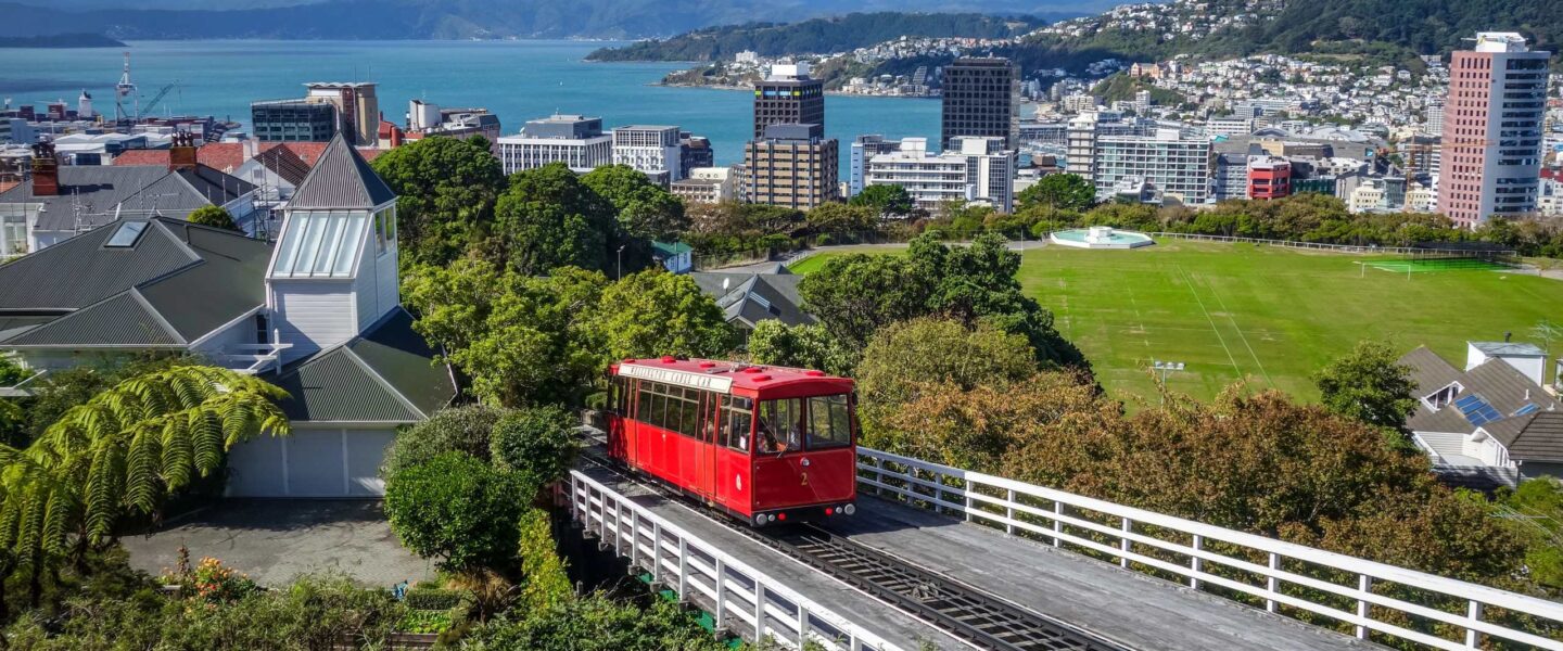 Zicht op Wellington en de zee vanaf de trambaan met een rode tram die naar beneden rijdt
