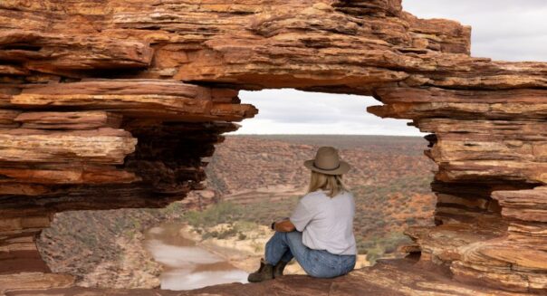Vrouw zit in het gat van Natures Window uit te kijken over de Murchison River in Kalbarri National Park