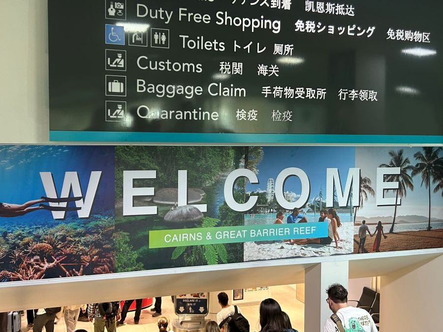 Welkomstbord op de luchthaven van Cairns met passagiers die aankomen die eronder doorlopen