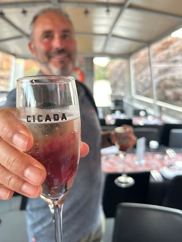 Peter laat een glas met een drankje met een hibiscus bloem zien tijdens de sunset tour in de Katherine Gorge