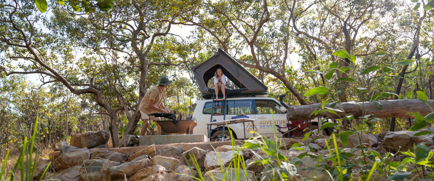 Vrouw zit in de daktent van een Adventure Rentals camper, man is hout aan het hakken