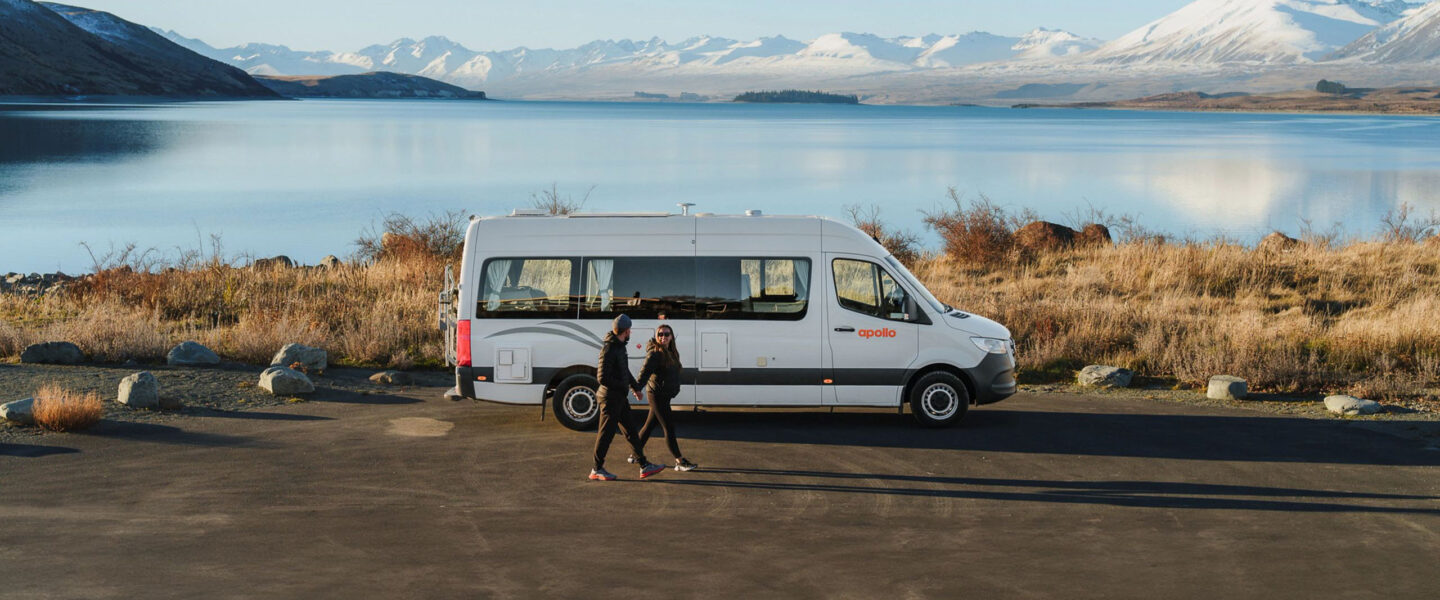Een koppel wandelt lang de Apollo Euro Plus camper die geparkeerd staat naast Lake Tekapo