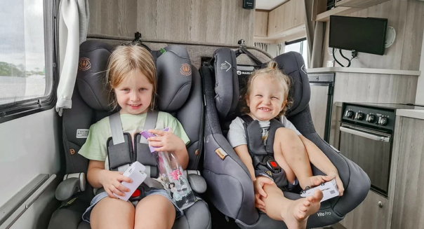 Twee jongere kinderen zitten in kinderautostoelen in de camper