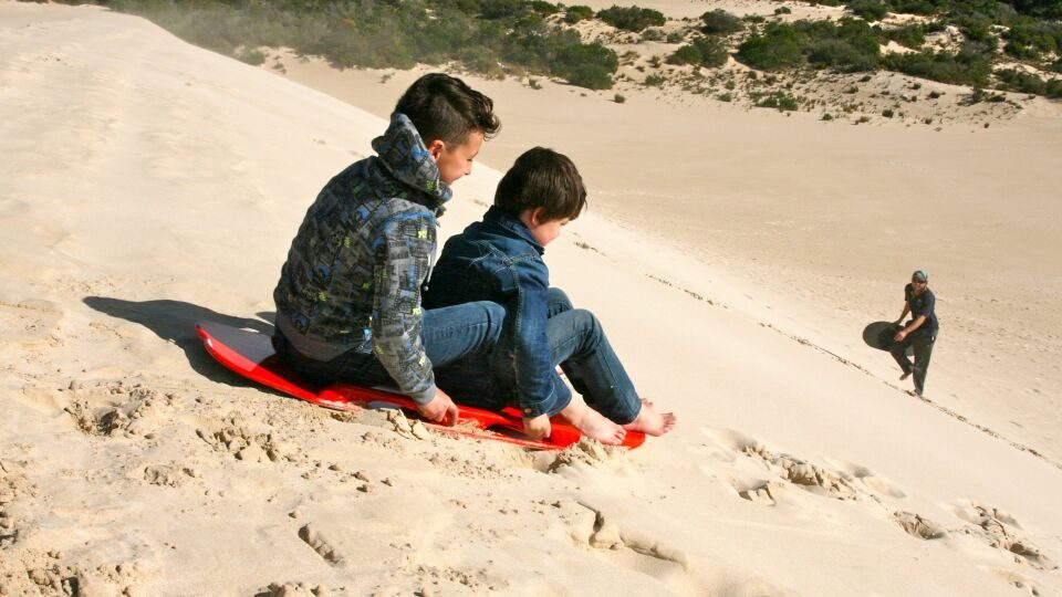 Twee jongens zijn aan het zandsurfen in de Little Sahara op Kangaroo Island