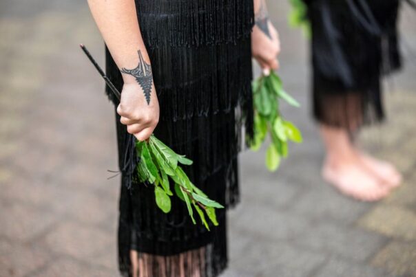 Maori vrouw draagt takken tijdens een powhiri openingsceremonie