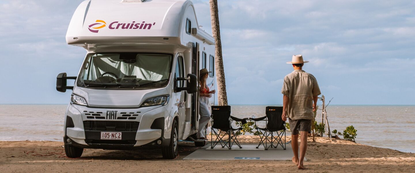 Man loopt naar Cruisin 6 Berth Deluxe camper die geparkeerd staat op een camingplek aan het strand