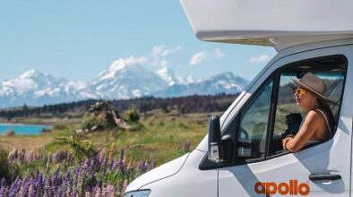 Apollo Euro Deluxe staat geparkeerd bij lupines op het Zuidereiland, vrouw kijkt naar buiten