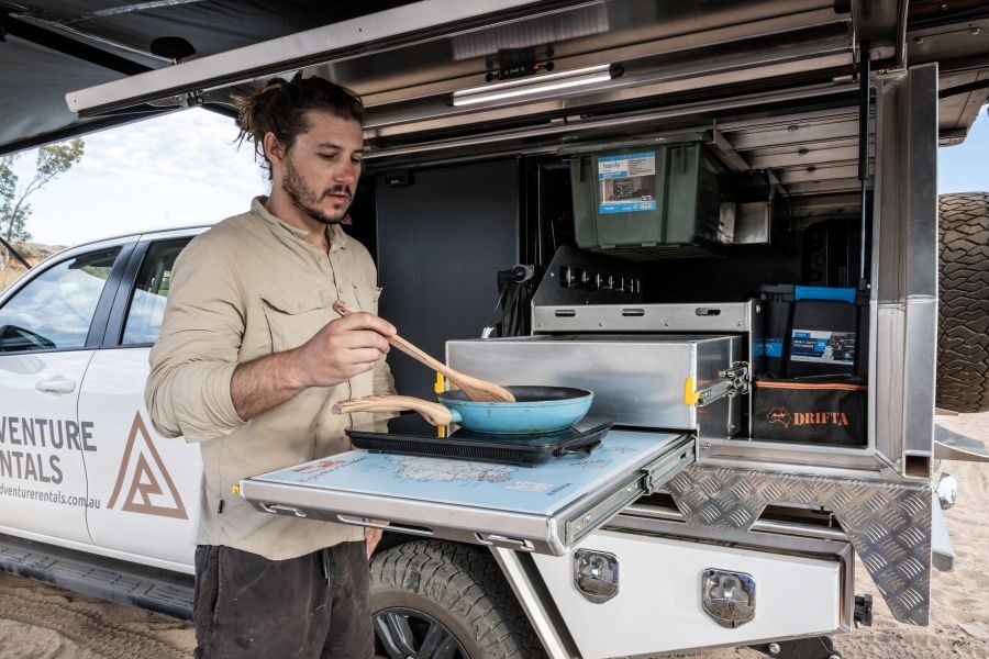 Man is aan het koken in de buitenkeuken van de Adventure Rentals Toyota Hilux 4WD