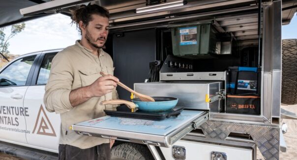 Man is aan het koken in de buitenkeuken van de Adventure Rentals Toyota Hilux 4WD