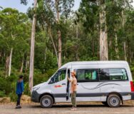 Apollo Endeavour staat geparkeerd in een bos in Australië, vrouw staat bij de open deur