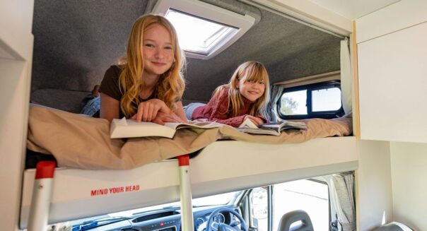 Twee kinderen liggen op het bed in de alkoof in de Apollo Euro Camper en kijken naar de fotograaf